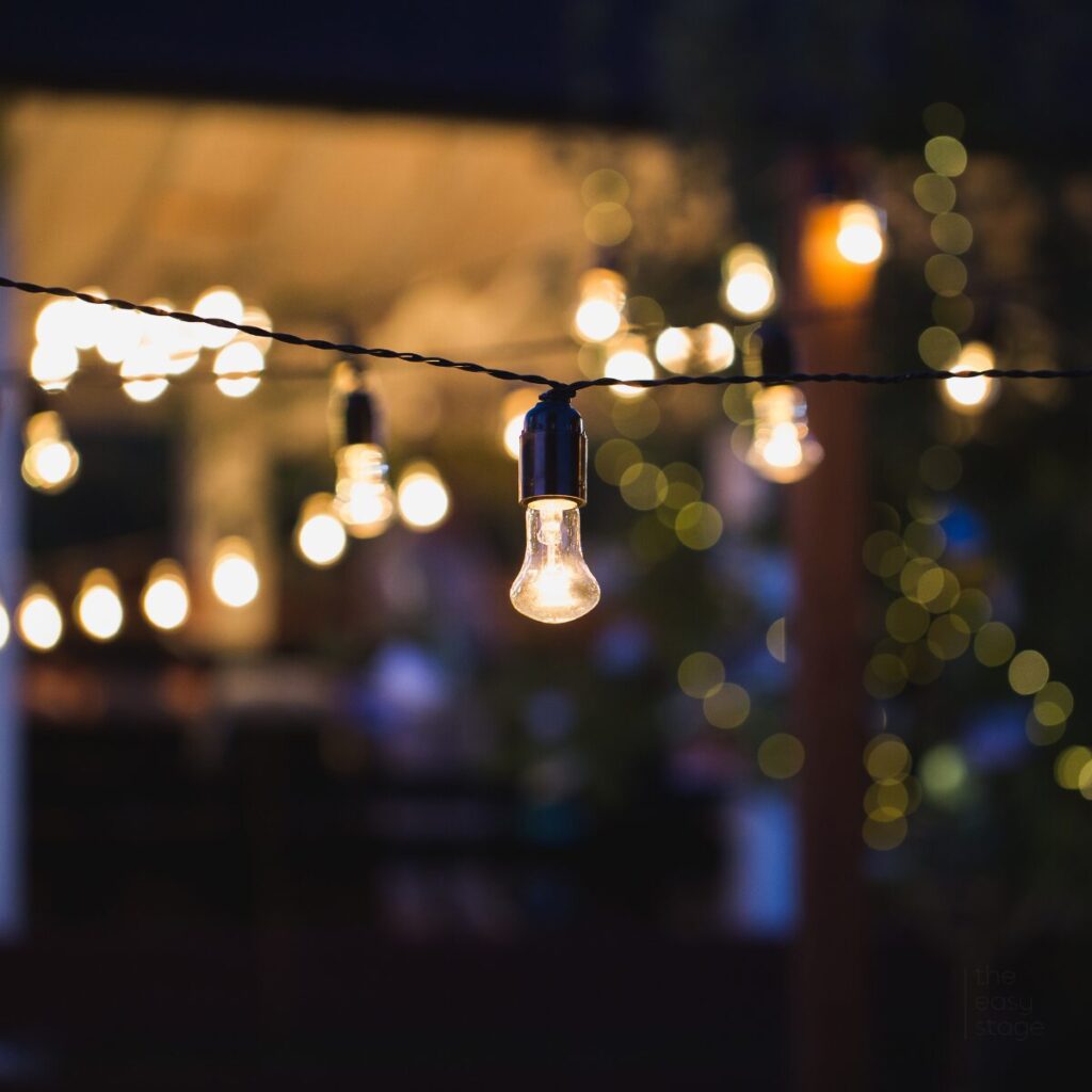 Outdoor string lights glowing above a cosy summer patio setting.