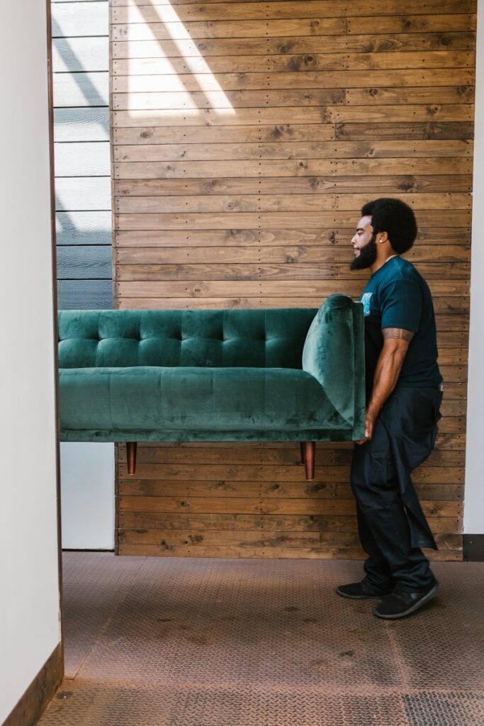 A stager carries a green sofa indoors, showcasing modern staging services